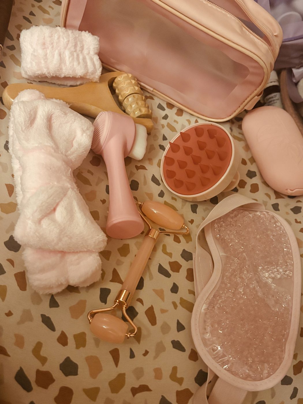 Le contenu de la trousse spa étalé : bandeaux éponge, rouleau massant en bois, brosse visage en silicone rose, brosse massante en silicone, rouleau visage et masque yeux en gel