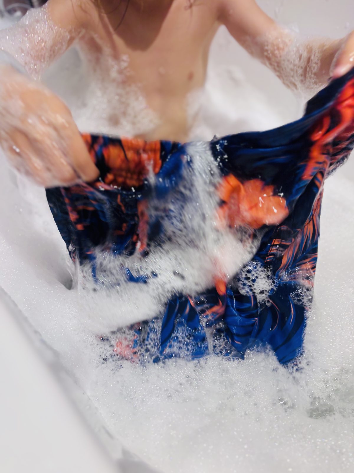 Des mains d'enfant frottent un maillot de bain savonné dans la mousse du bain