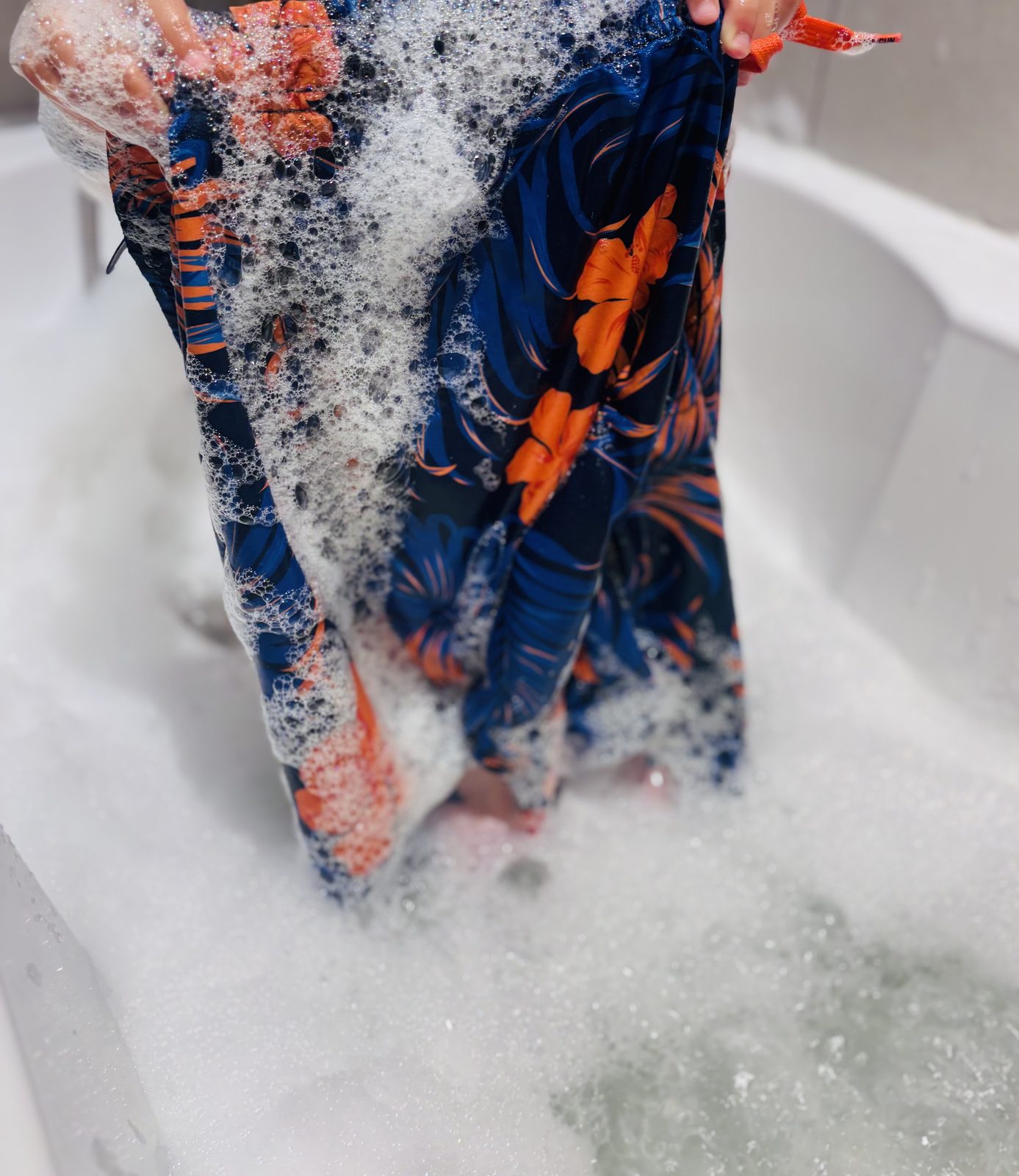 Un enfant dans le bain brandit un maillot de bain couvert de mousse à bout de bras