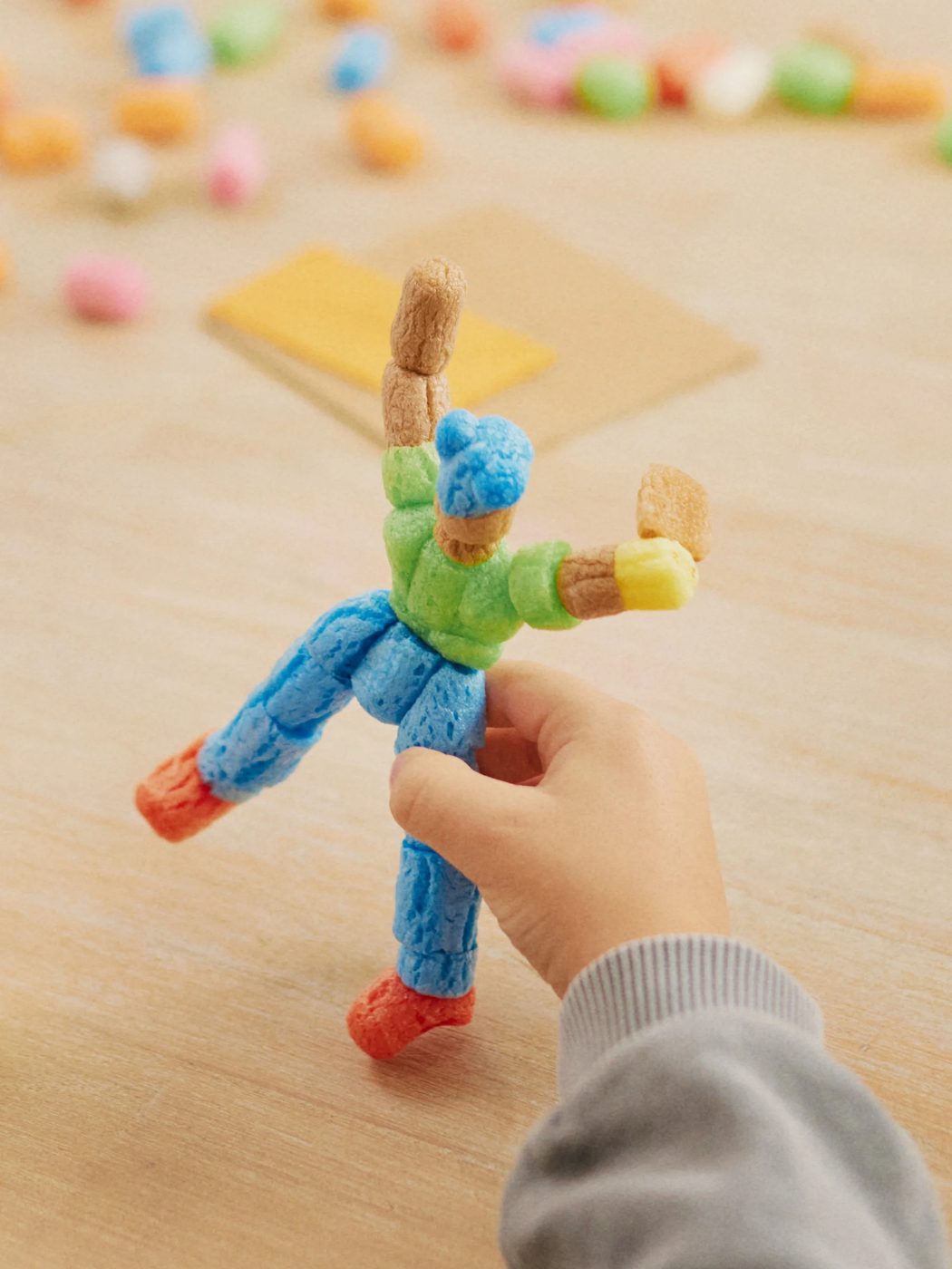 Un petit bonhomme articulé construit en flocons de PlayMaïs, tenu dans une main