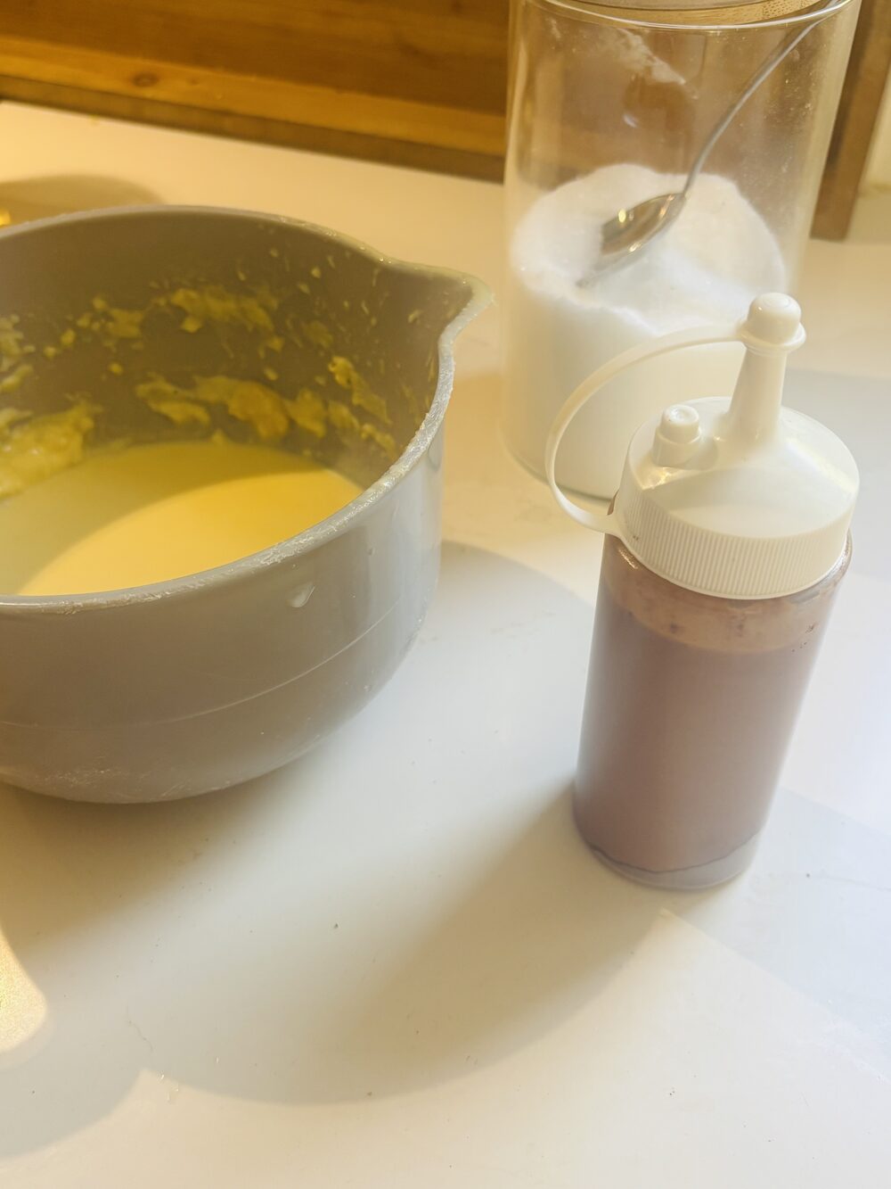 Un saladier de pâte à crêpes nature posé à côté d'une bouteille souple remplie de pâte au chocolat, prêtes pour le marbrage
