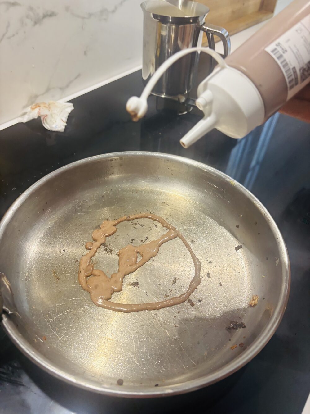 Un cercle de pâte au chocolat dessiné à la bouteille souple au fond d'une poêle, la bouteille posée juste au-dessus