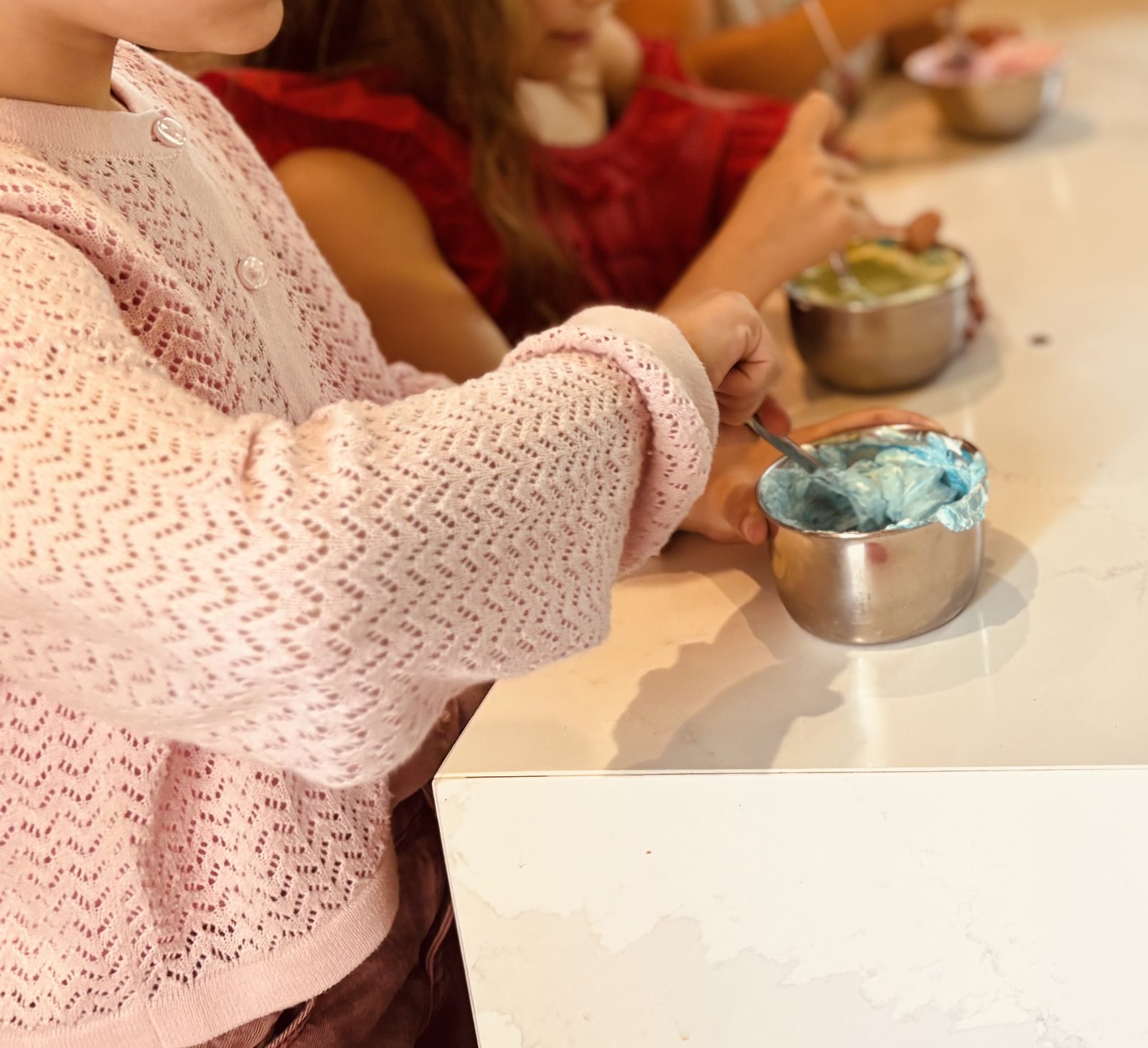 Une enfant mélange une pointe de colorant dans un petit bol de chantilly, obtenant un joli bleu
