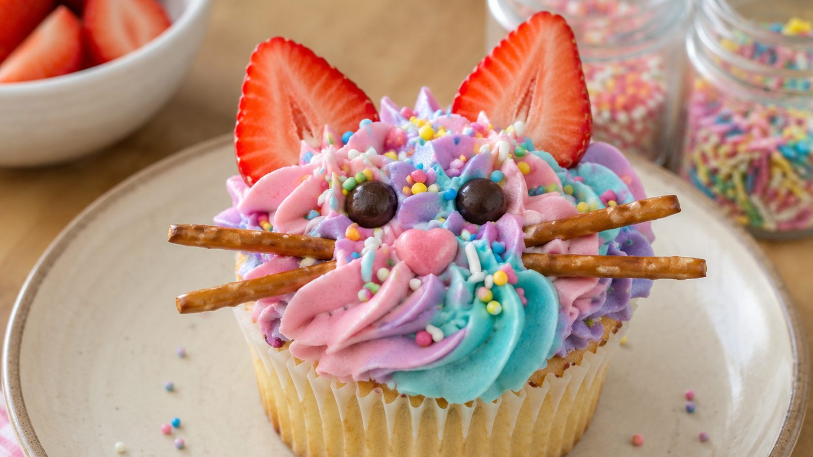Un cupcake décoré en tête de chat avec des fraises, des bretzels et de la chantilly colorée