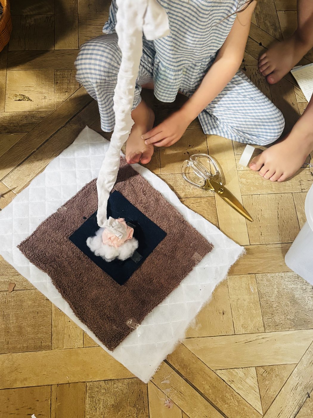 Une enfant installe au sol son système d'amortissement pour le défi de l'oeuf : un matelas moelleux, une serviette pliée en losange et un nid de coton au centre, où l'oeuf sera placé avant la chute
