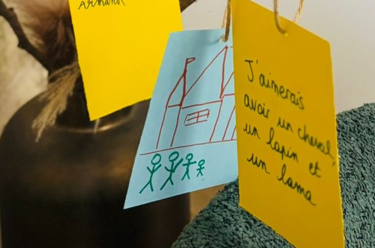 Deux étiquettes accrochées à notre arbre : une étiquette bleue avec un dessin d'enfant représentant une maison et une famille en bonshommes bâtons, et une étiquette orange avec un souhait écrit à la main