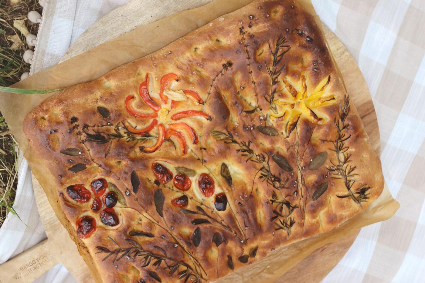 La focaccia jardin une fois cuite et dorée, posée sur une planche en bois pour le pique-nique