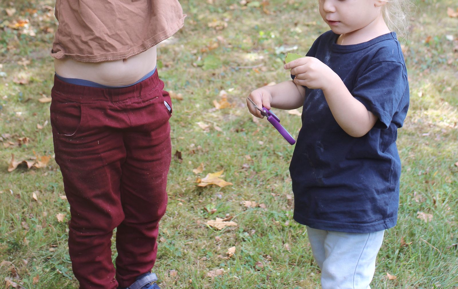 Une petite fille découpe soigneusement une feuille avec des ciseaux d'écolier dans le jardin