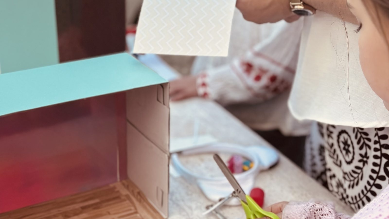 Un enfant tapisse les murs de la boîte avec du papier à motifs pendant qu'un adulte découpe