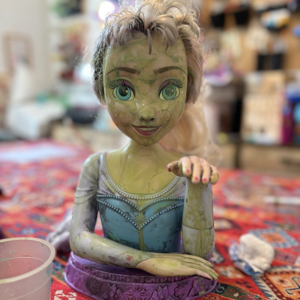 Tête de poupée Reine des neiges au visage entièrement peint en vert, on dirait Shrek
