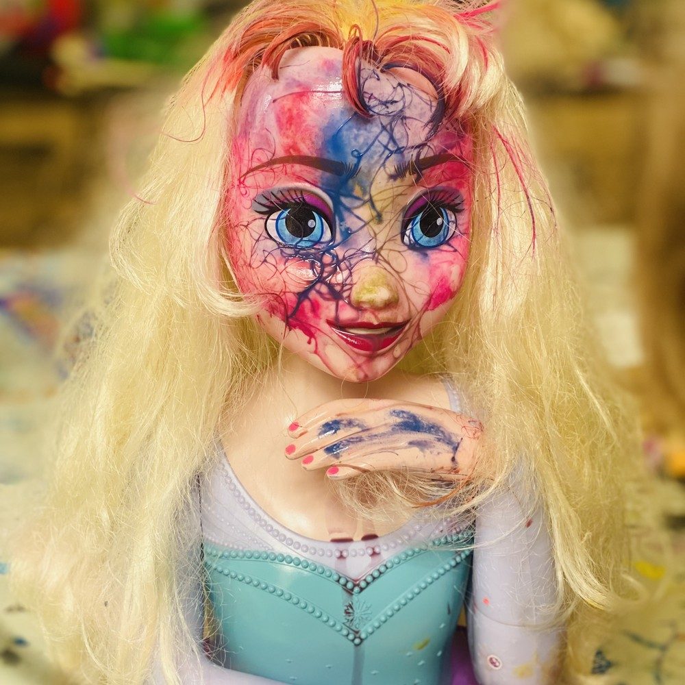 Tête de poupée blonde au visage peint de rose et de bleu façon abstrait