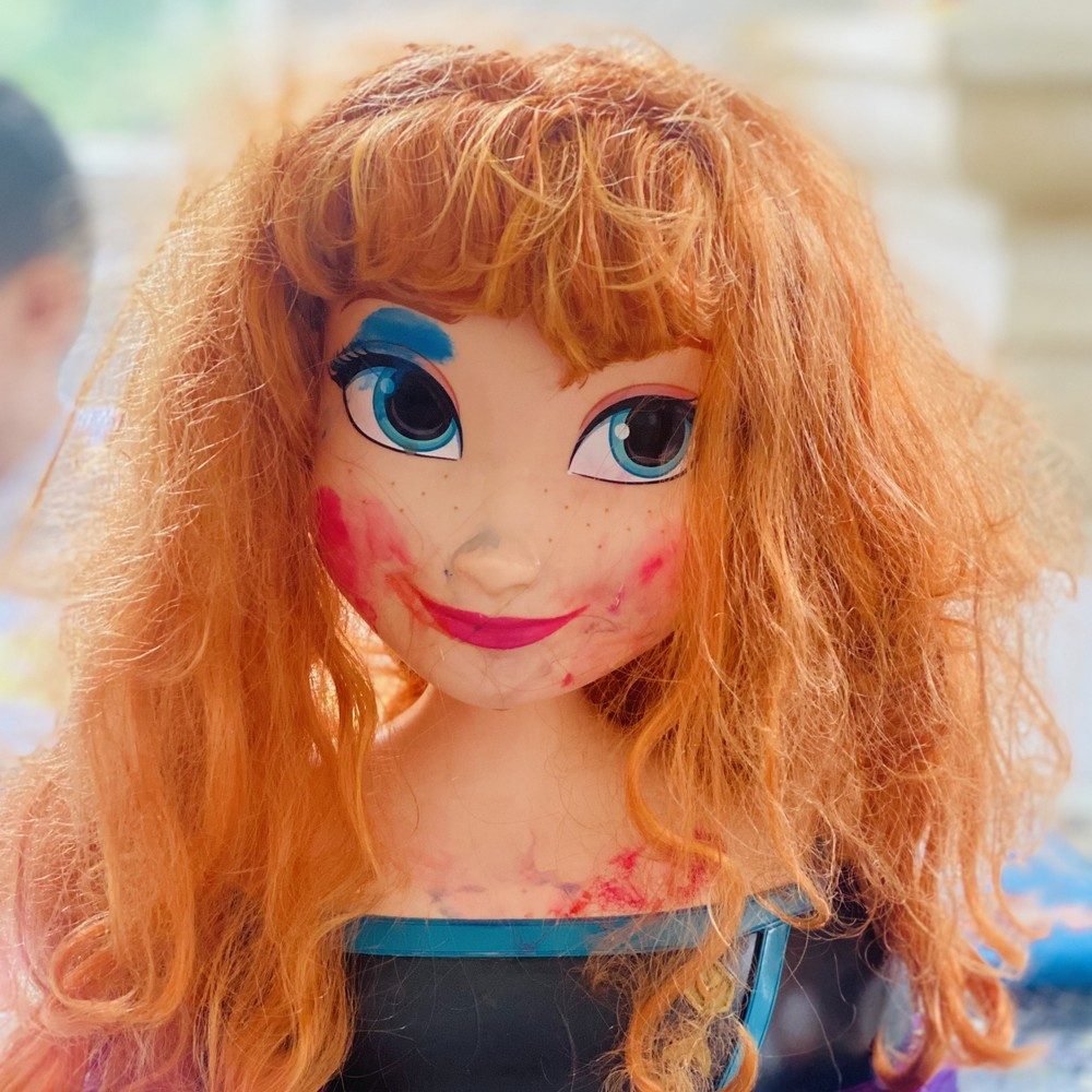 Tête de poupée rousse avec du rouge à lèvres qui déborde et un fard bleu sur les sourcils