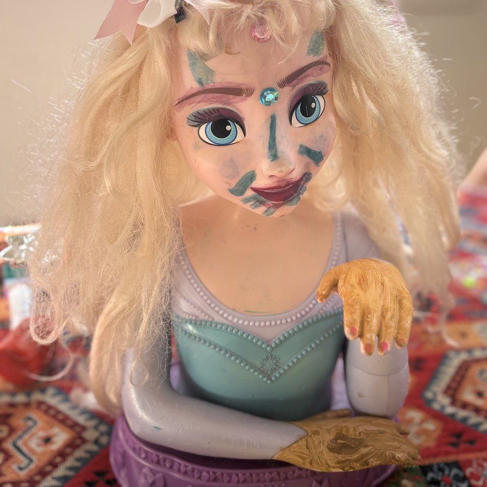 Tête de poupée blonde au visage peint de motifs bleus avec un faux bijou collé sur le front