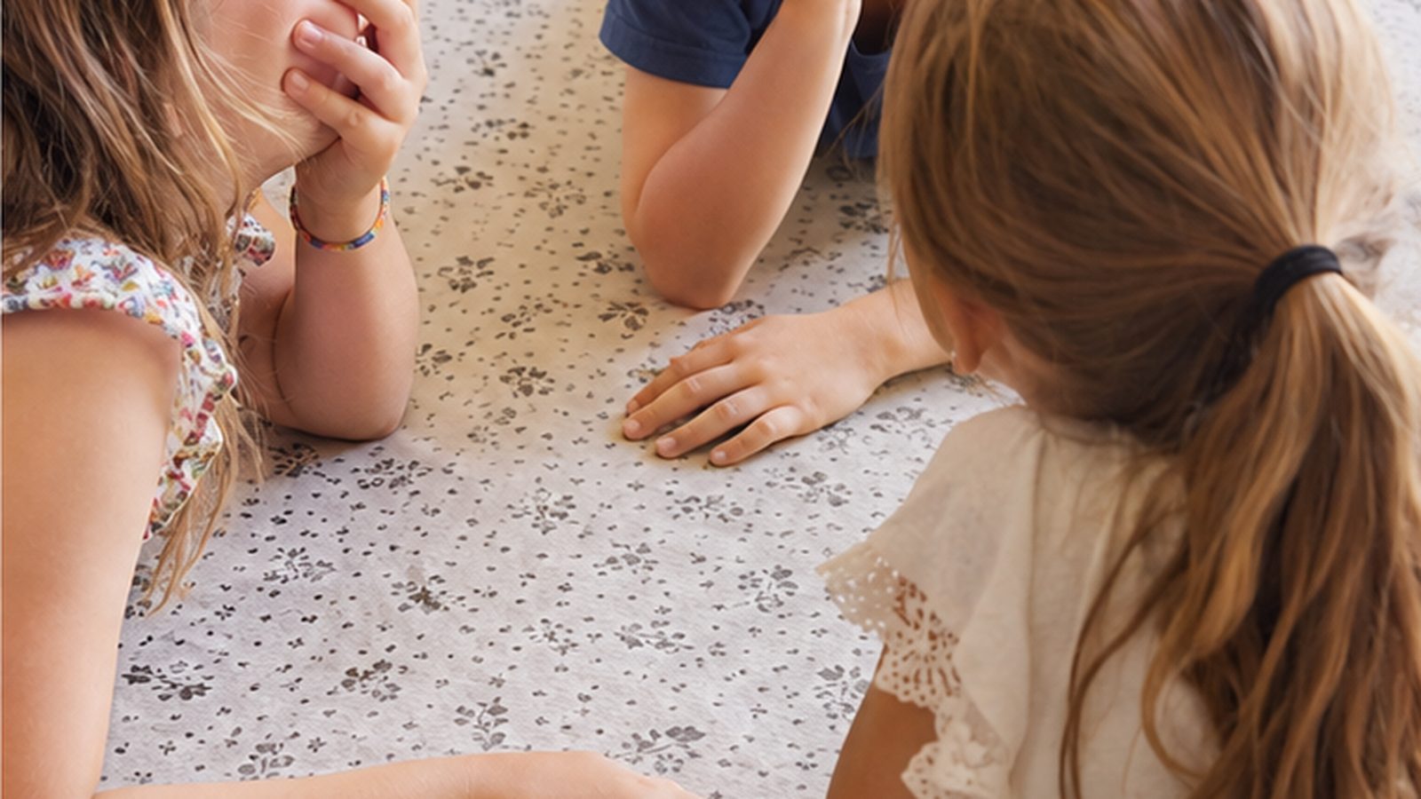 Une enfant plaque ses mains sur sa bouche pendant une partie de ni oui ni non, entourée de deux autres enfants allongés sur le tapis