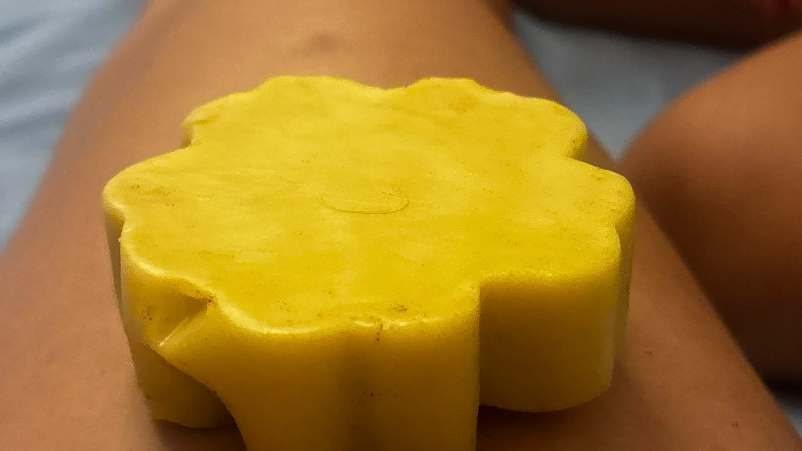 Barre de massage jaune en forme de fleur posée sur une jambe, prête à l'emploi