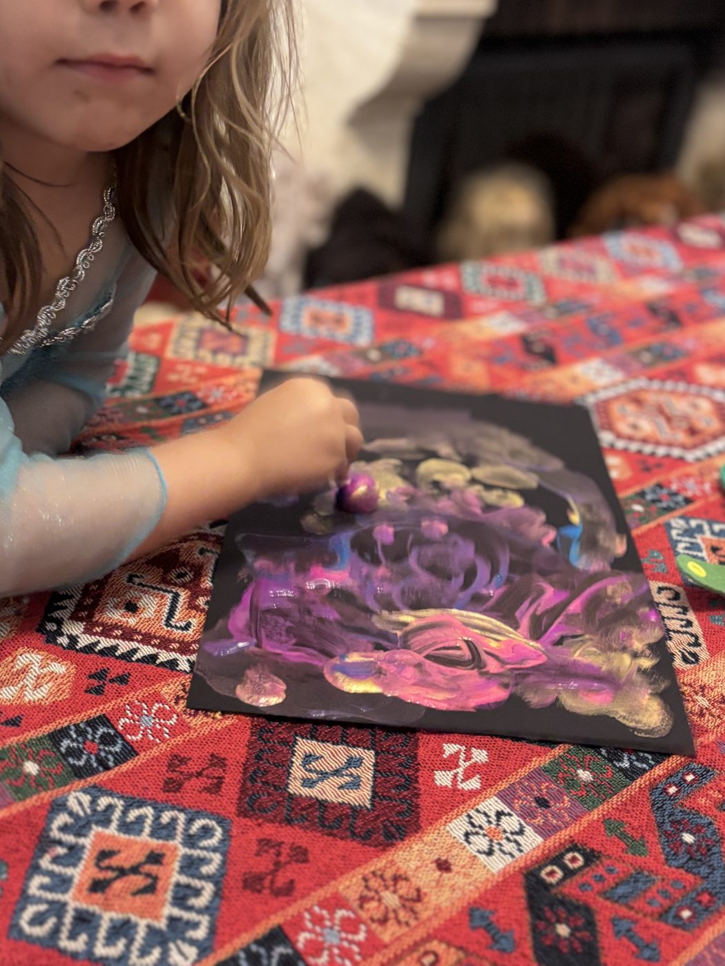 Une petite fille tamponne de la peinture violette et dorée au doigt sur sa feuille noire, à côté d'une nébuleuse déjà bien remplie
