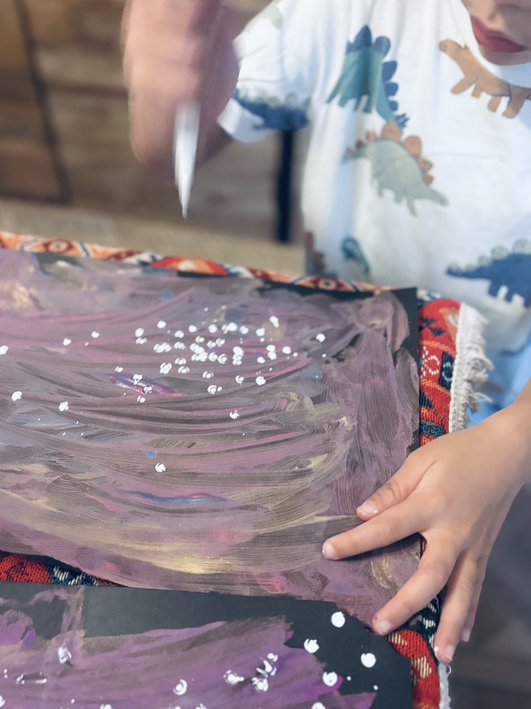 Un enfant tient un marqueur blanc au-dessus de sa galaxie violette et dorée, déjà constellée de petits points blancs