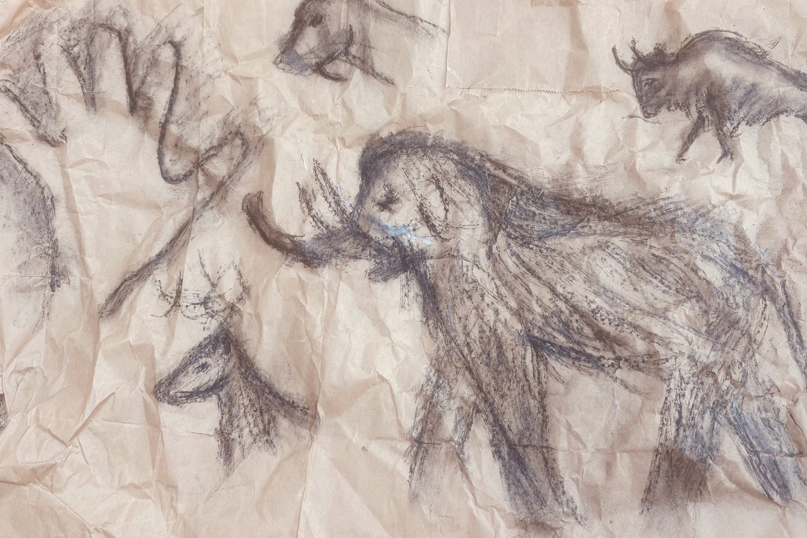 Grande fresque au charbon sur papier kraft froissé : un mammouth au centre avec ses défenses recourbées, un cerf, un bison et un rhinocéros