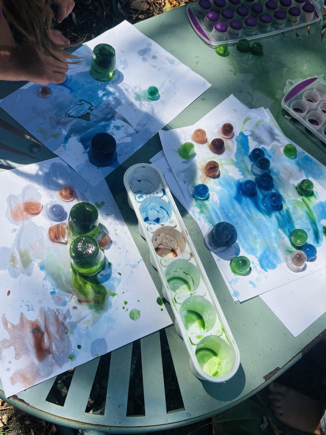 Coin de jardin à l'ombre d'un grand arbre, l'atelier peinture installé sur une table en arrière-plan