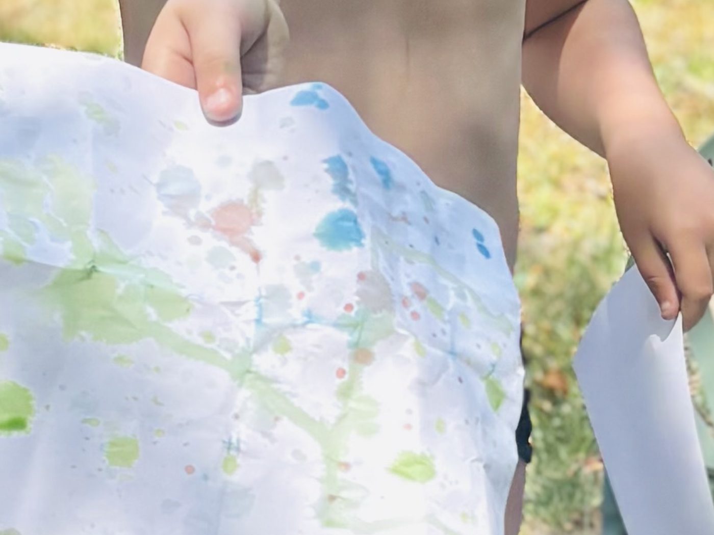 Une feuille éclaboussée de peinture verte et bleue brandie à bout de bras, dans le jardin ensoleillé