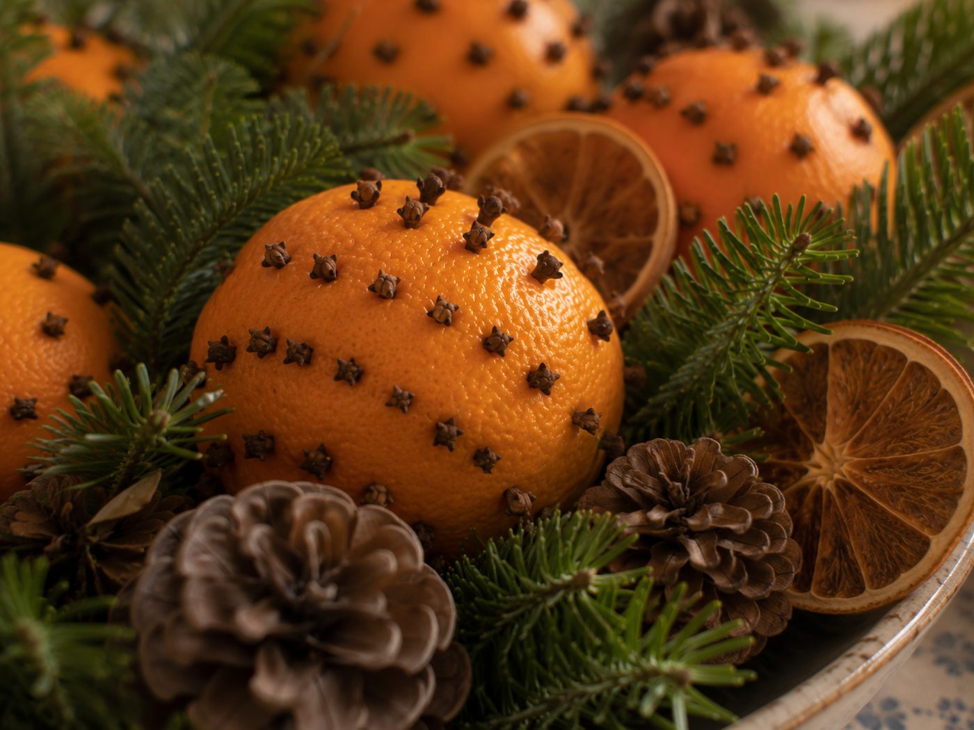 Gros plan d'une corbeille d'oranges piquées de clous de girofle mêlées à des branches de sapin, des pommes de pin et des tranches d'orange séchées