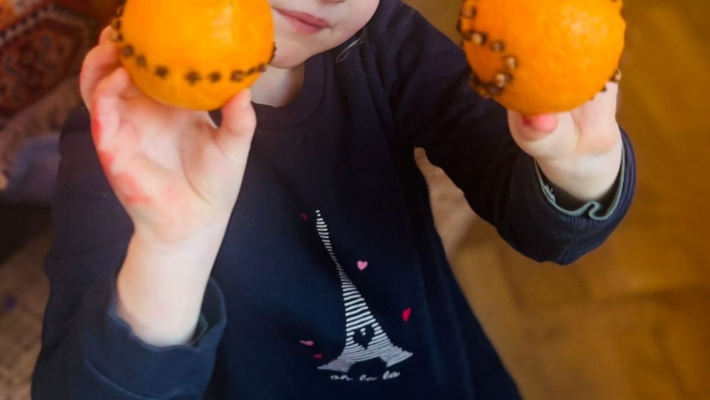 Une enfant présente deux oranges piquées de clous de girofle formant de jolis motifs, tenues à hauteur de visage