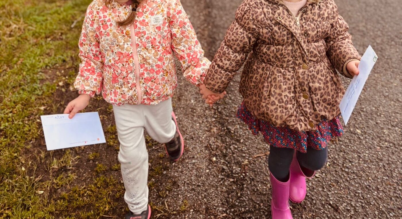 Deux enfants marchant main dans la main sur une route de campagne, chacun tenant une enveloppe