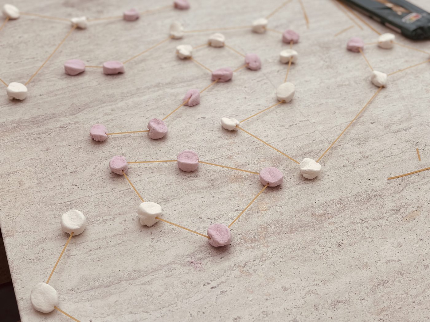 Plusieurs constellations reproduites à plat sur une table en pierre avec des chamallows roses et blancs reliés par des spaghettis crus