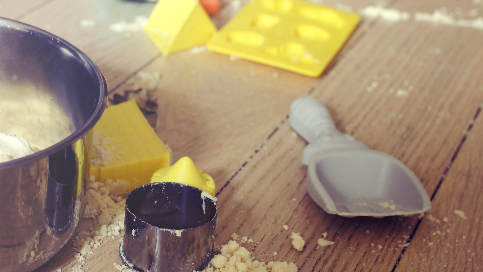 Miettes de sable magique éparpillées sur un parquet, avec moules en plastique, emporte-pièces et petite pelle