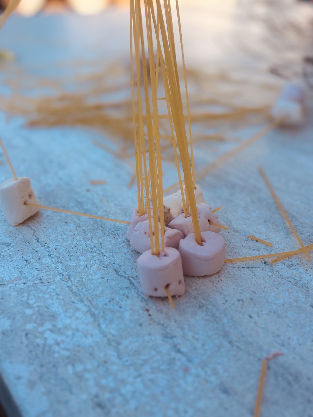 Gros plan sur la base d'une tour : plusieurs chamallows roses au sol dans lesquels convergent une dizaine de spaghettis