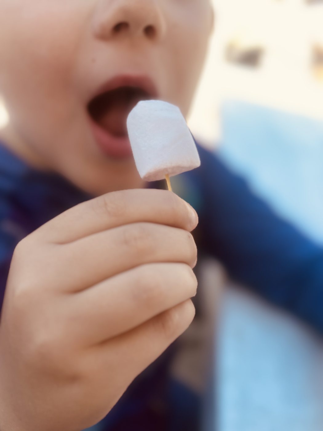 Gros plan sur une main d'enfant tenant un chamallow planté sur un spaghetti, porté vers sa bouche
