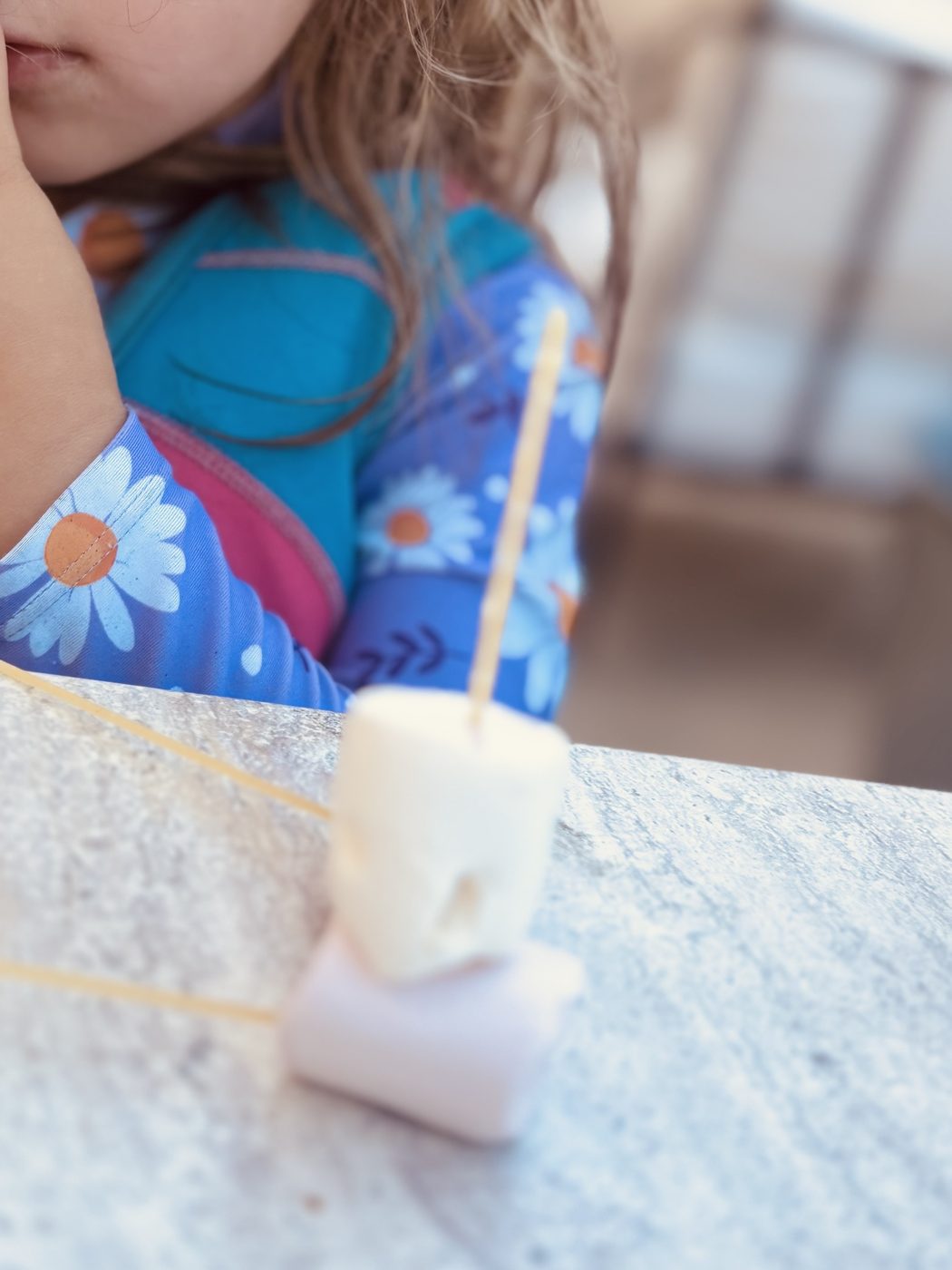 Une enfant accoudée à la table, immobile devant deux chamallows empilés sur un spaghetti