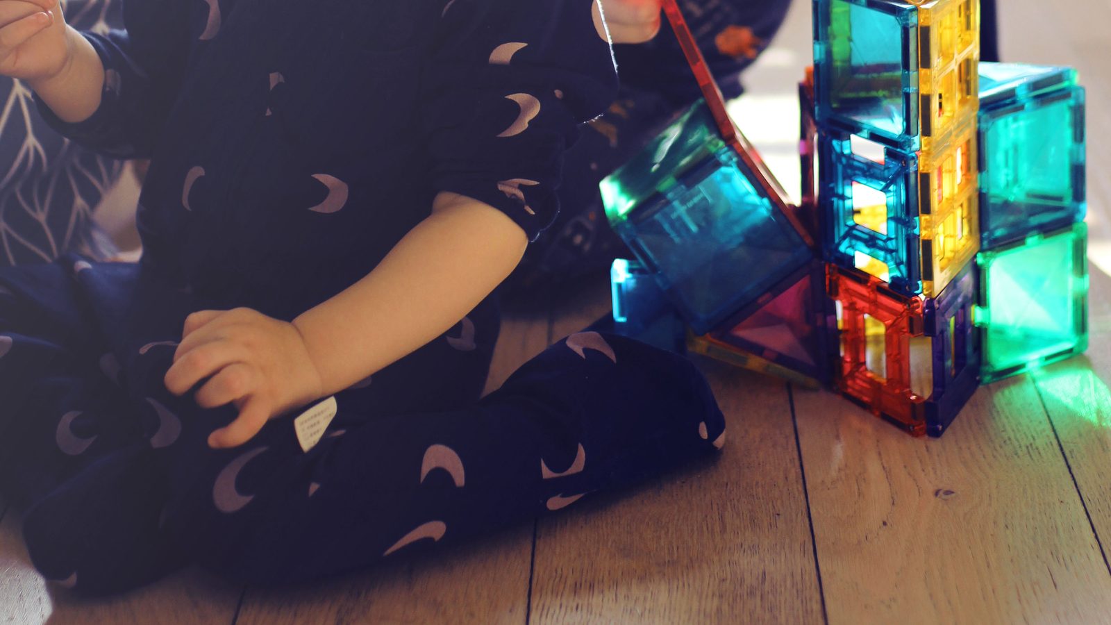 Deux enfants en pyjama assis sur le parquet, en train de construire une tour en tuiles magnétiques colorées dans la lumière du matin