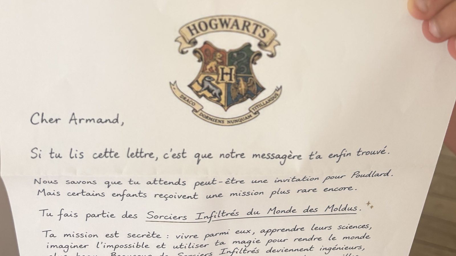 Un enfant tout sourire tenant la lettre au sceau de Poudlard reçue à son prénom