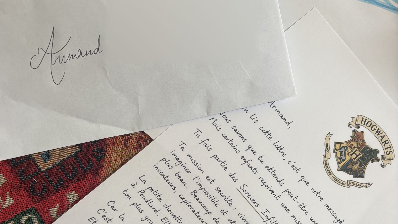 Une enveloppe manuscrite au prénom d'un enfant, posée à côté d'une lettre au sceau de Poudlard sur un tapis coloré