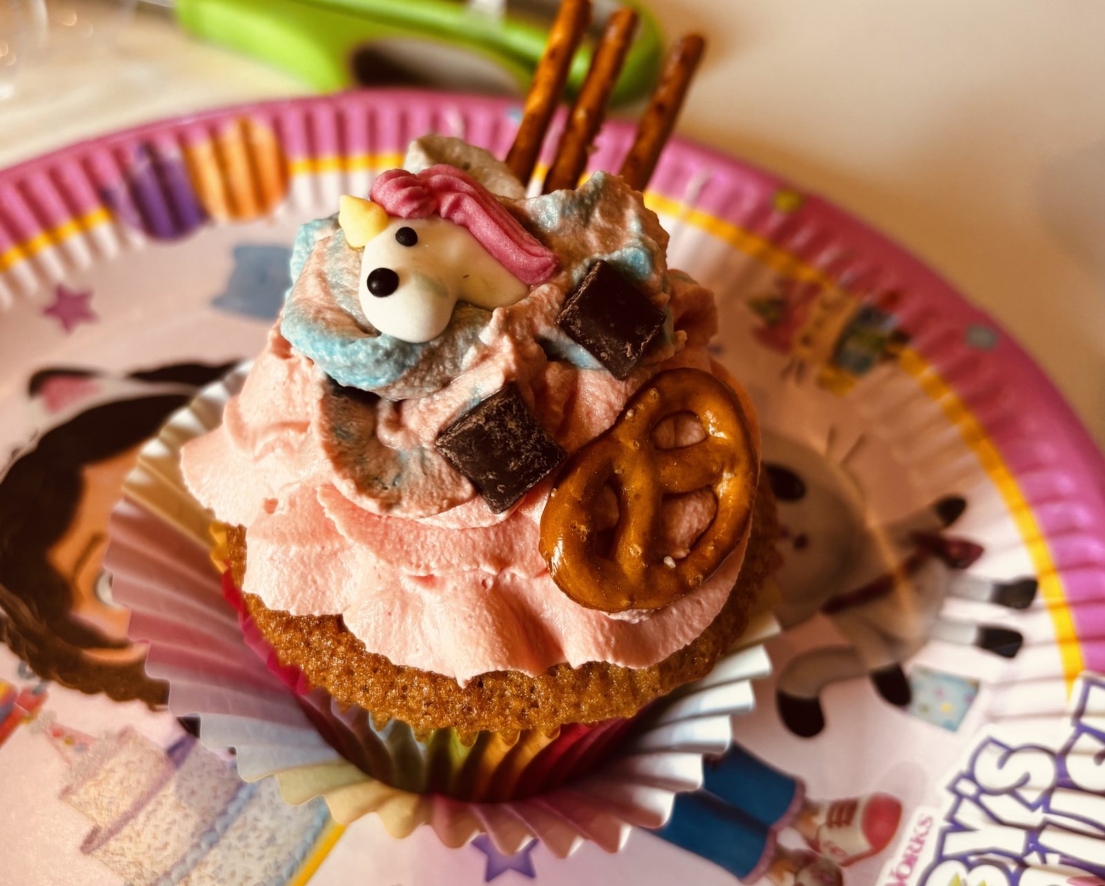 Un cupcake-chat décoré à la chantilly rose, bretzel en moustache et petit chat en sucre, sur une assiette Gabby