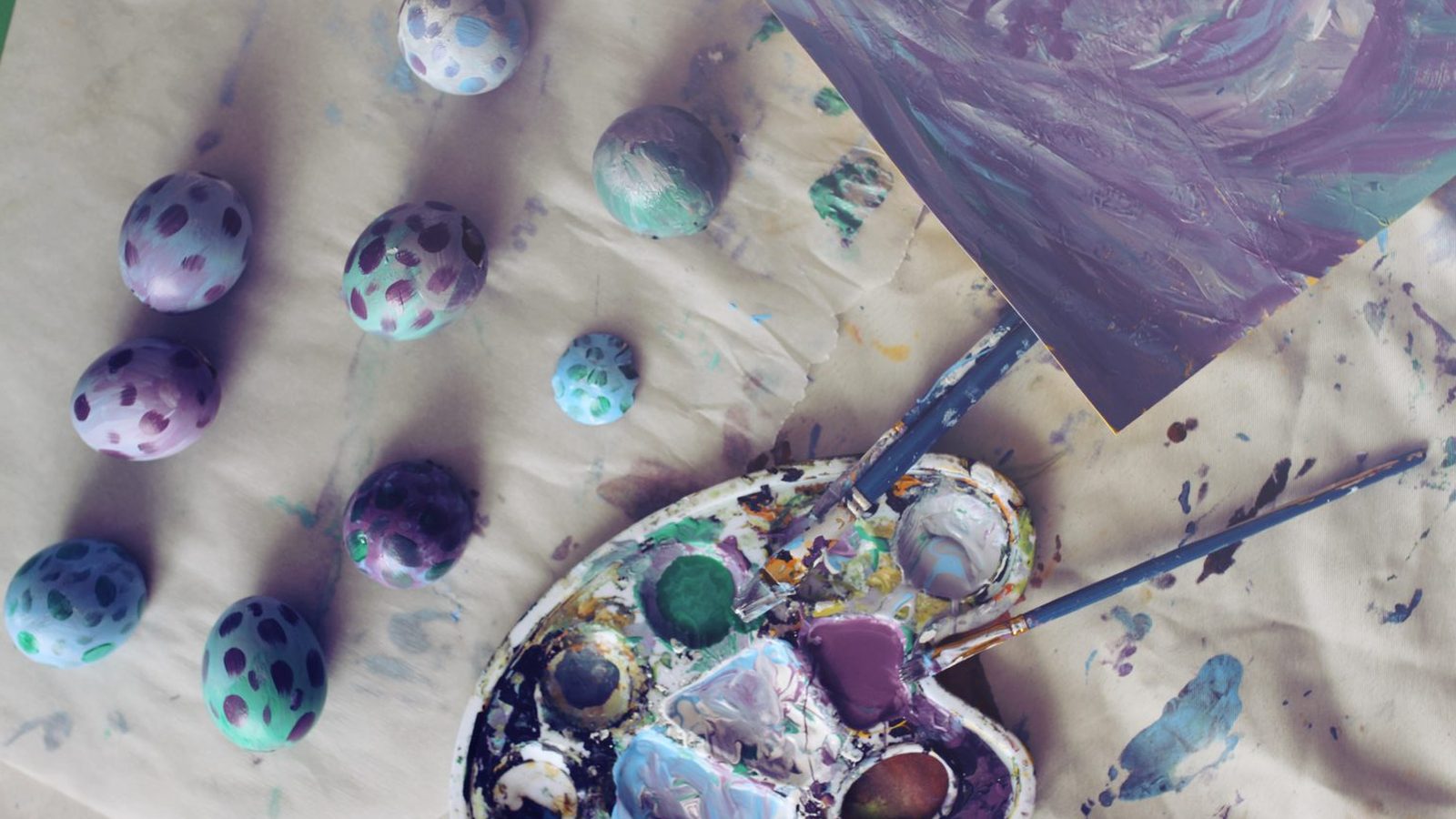Œufs de dragon peints en bleu et violet par les enfants, posés sur la nappe à côté de la palette de peinture